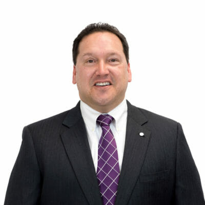 Chip Umberger at Bank of the James wearing a dark grey suit jacket, white button down shirt and purple tie with a lapel pin