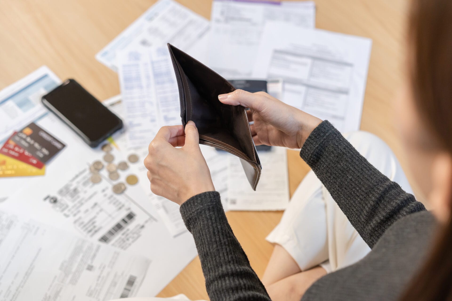 Woman sitting on the floor holding open an empty wallet with personal documents surrounding her