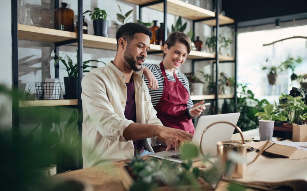 Man and woman shop assistants with laptop working in indoor potted plant store.